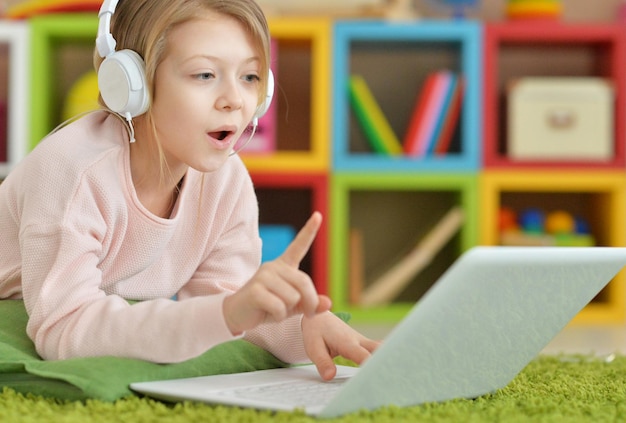 Menina bonitinha em fones de ouvido usando laptop