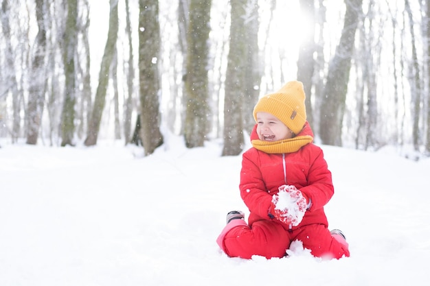 Menina bonitinha em roupa de neve rosa brinca com neve na floresta de inverno