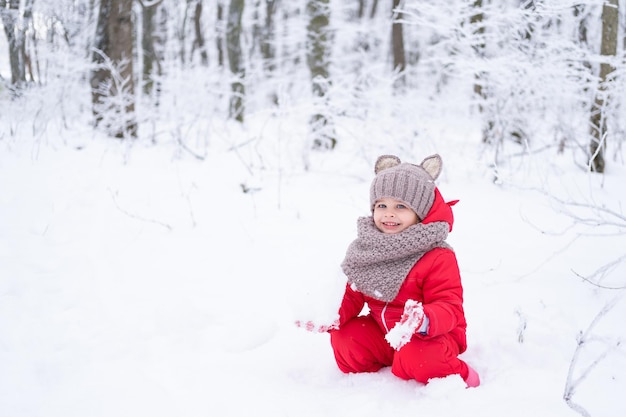 Menina bonitinha em roupa de neve rosa brinca com neve na floresta de inverno