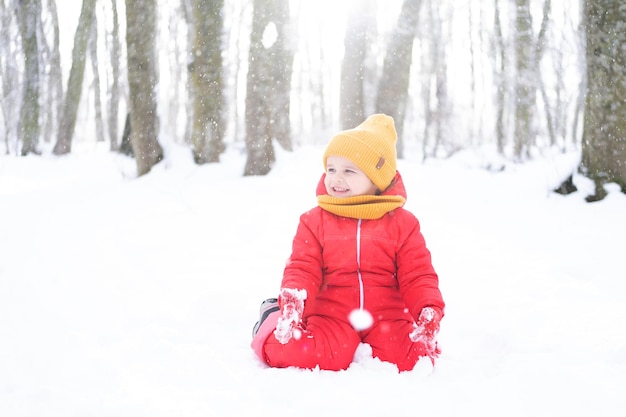 Menina bonitinha em roupa de neve rosa brinca com neve na floresta de inverno