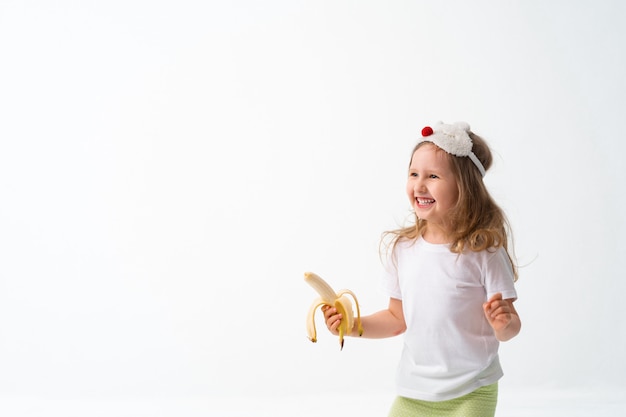 Menina bonitinha em roupas casuais, segurando uma banana na mão isolar