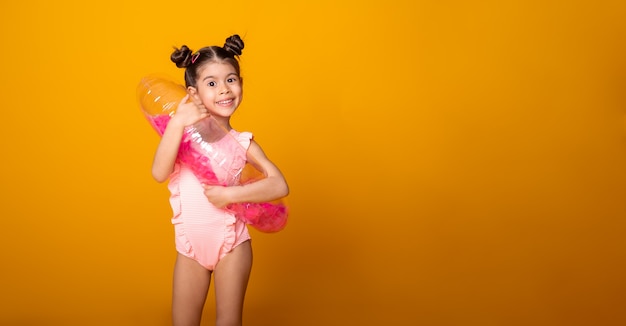 Menina bonitinha em traje de banho e anel inflável de natação sorrindo sobre fundo amarelo. banner copyspace.