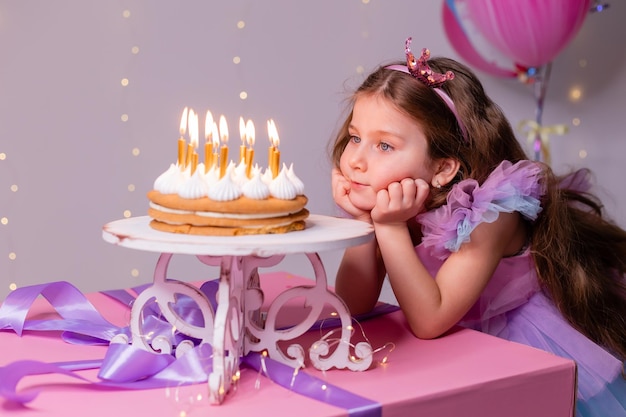 Menina bonitinha em um lindo vestido faz um desejo e sopra as velas no bolo de aniversário