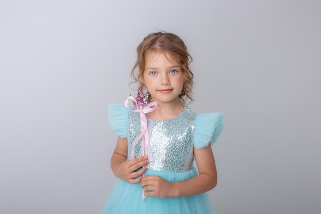 Menina bonitinha em um lindo vestido segurando uma varinha mágica de fada em um fundo branco