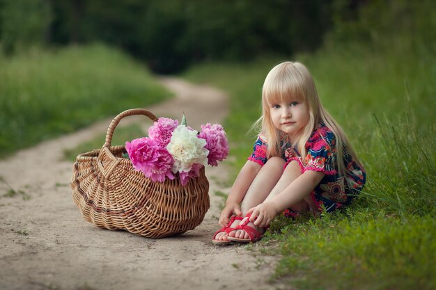 Menina bonitinha em uma estrada florestal com uma cesta de flores no dia de verão ao ar livre