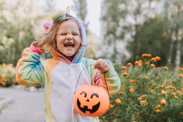 Menina bonitinha em uma fantasia de unicórnio arco-íris para a criança de Halloween caminhando em uma travessura ou travessura ao ar livre