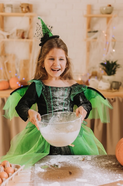 Menina bonitinha em uma fantasia verde de Halloween de uma bruxa ou fada preparando uma torta de abóbora