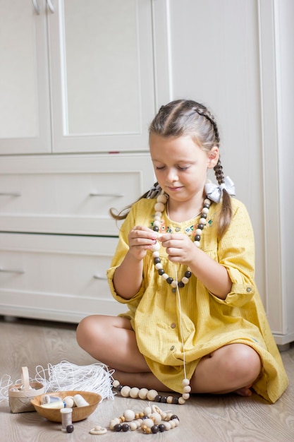 Menina bonitinha enfiando contas e fazendo joias ecologicamente corretas