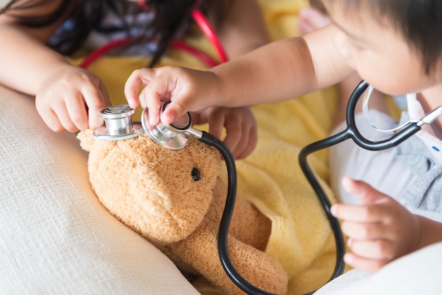 Menina bonitinha está brincando de médico com estetoscópio e ursinho de pelúcia.