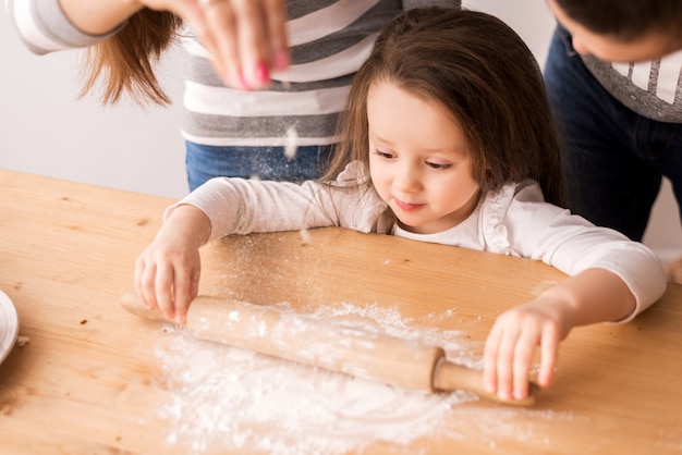 Menina bonitinha está cozinhando na cozinha. estende a massa com farinha em biscoitos e pães