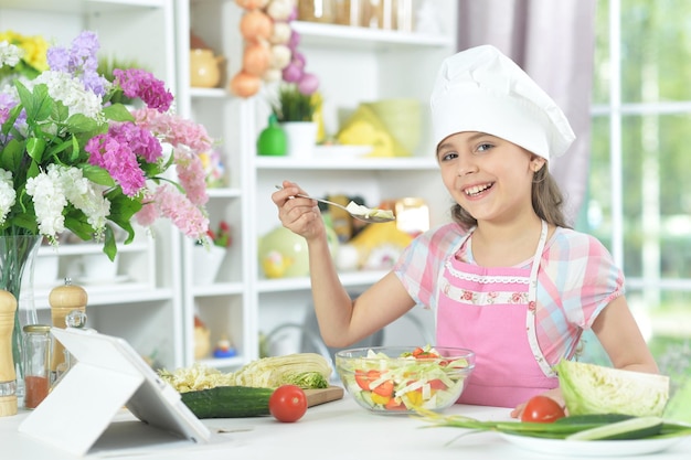 Menina bonitinha fazendo jantar na mesa da cozinha em casa