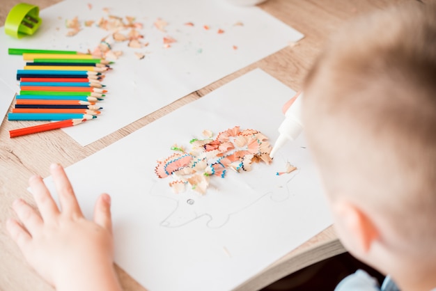 Menina bonitinha fazer apliques colas casa colorida, aplicando papel de cor usando cola ao fazer artes e ofícios na pré-escola ou em casa. Idéia para a criatividade das crianças, um projeto de arte feito de papel.