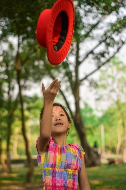 Menina bonitinha jogando um chapéu vermelho em um parque verde de verão.