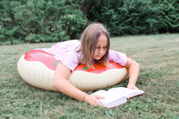 Menina bonitinha lendo livro ao ar livre. Descanso de verão