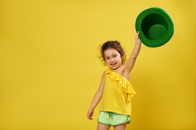 Menina bonitinha levanta a mão segurando um chapéu irlandês de duende verde.