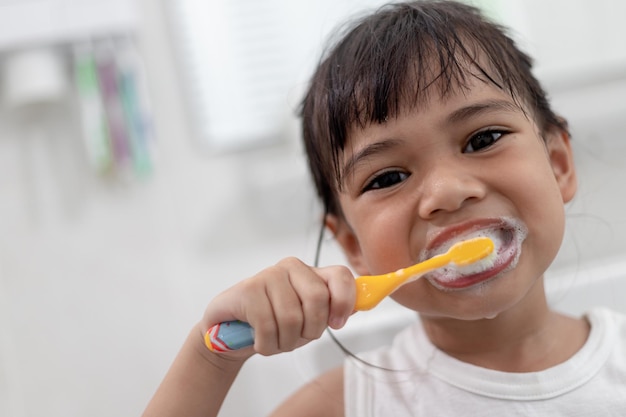 Menina bonitinha limpando os dentes com uma escova de dentes no banheiro