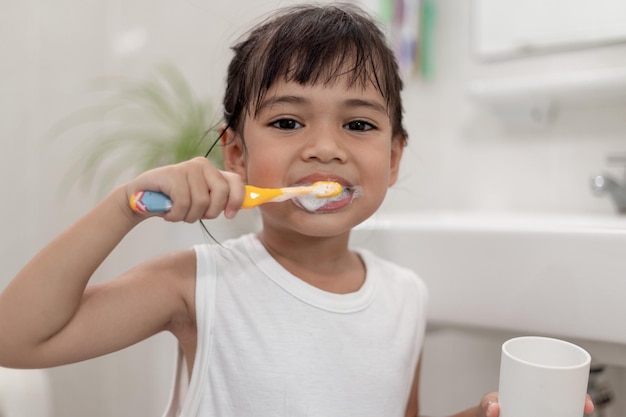 Menina bonitinha limpando os dentes com uma escova de dentes no banheiro