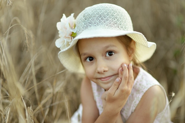 Menina bonitinha no campo de trigo de verão ao pôr do sol