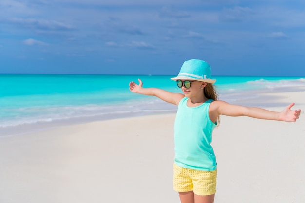 Menina bonitinha no chapéu andando na praia durante férias nas Caraíbas