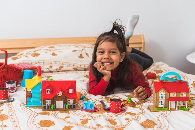 Menina bonitinha no suéter vermelho de gola longa t-shirt brincando com seus brinquedos no quarto.