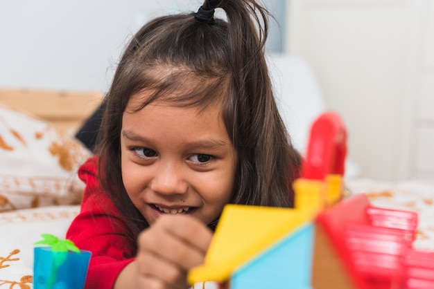 Menina bonitinha no suéter vermelho de gola longa t-shirt brincando com seus brinquedos no quarto.