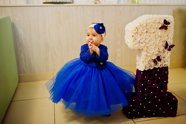 Menina bonitinha no vestido azul perto do número de aniversário de 1 ano