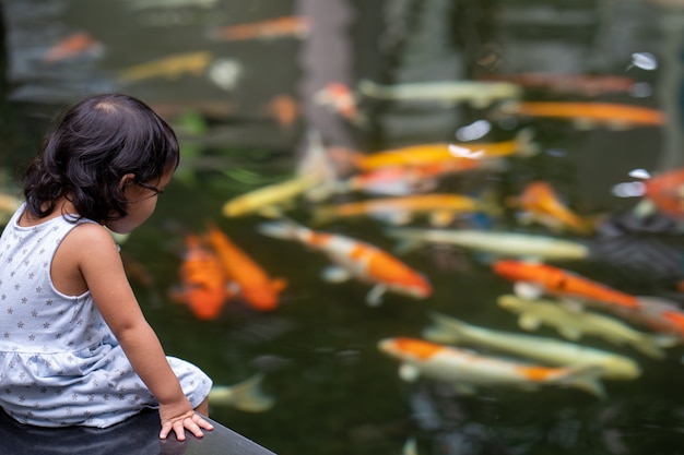 Menina bonitinha olhando peixes carpas koi