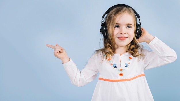 Menina bonitinha ouvindo música no fone de ouvido apontando o dedo para algo