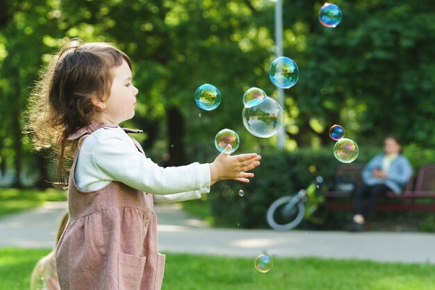 Menina bonitinha pegando bolhas de sabão em um parque da cidade