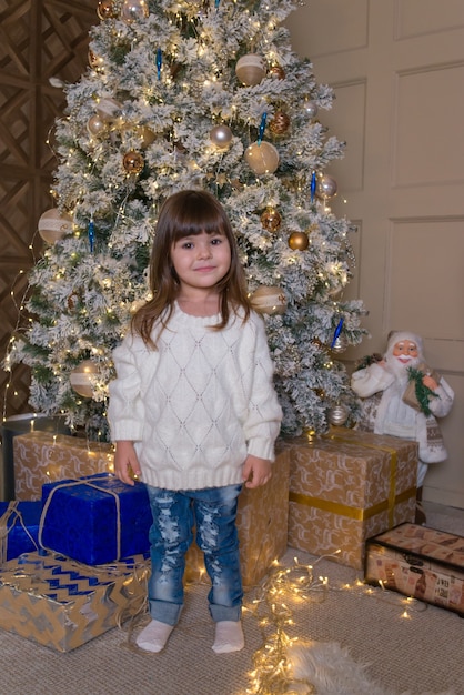 menina bonitinha perto da árvore de natal com presentes