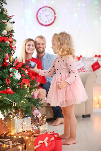 Menina bonitinha perto da árvore de Natal e seus pais felizes no fundo