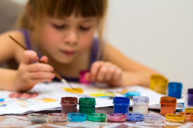 Menina bonitinha pintando com pincel e tintas coloridas