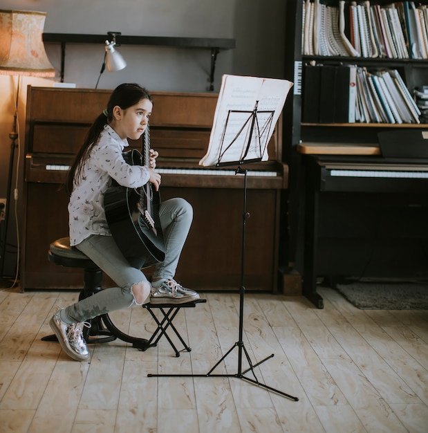 Foto menina bonitinha praticando em um violão em casa