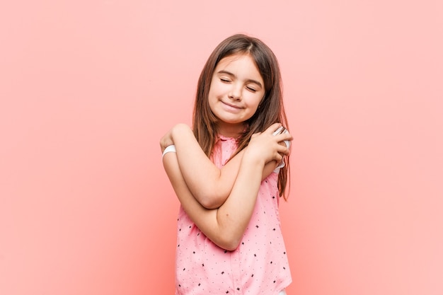 Menina bonitinha se abraça, sorrindo despreocupada e feliz.