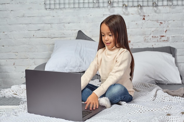 Menina bonitinha se divertindo enquanto assiste desenhos em um laptop sentada na cama