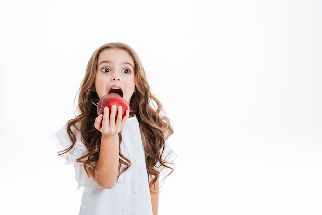 Menina bonitinha segurando e comendo maçã vermelha