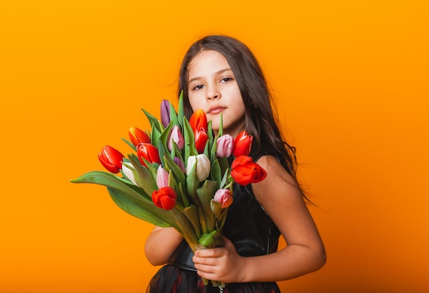 Menina bonitinha segurando um buquê de tulipas em um fundo amarelo Feliz dia das mulheres Lugar para texto Emoções vívidas 8 de março