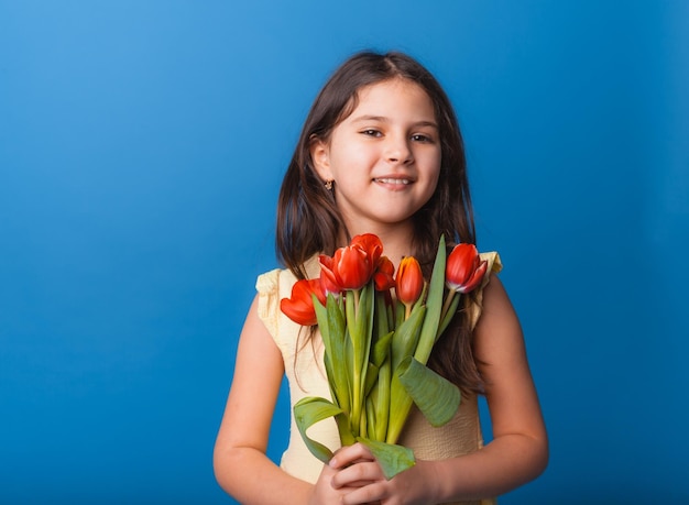 Menina bonitinha segurando um buquê de tulipas em um fundo azul Feliz dia das mulheres Lugar para texto Emoções vívidas 8 de março