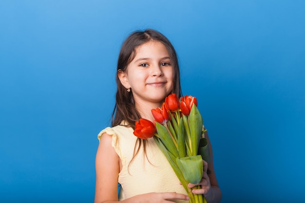 Menina bonitinha segurando um buquê de tulipas em um fundo azul Feliz dia das mulheres Lugar para texto Emoções vívidas 8 de março