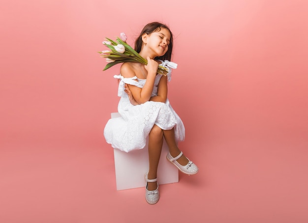 Menina bonitinha segurando um buquê de tulipas em um fundo rosa Feliz dia das mulheres Lugar para texto Emoções vívidas 8 de março