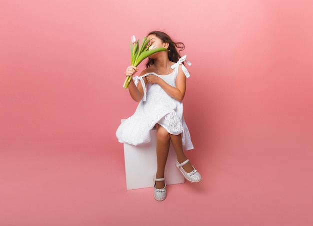 Menina bonitinha segurando um buquê de tulipas em um fundo rosa Feliz dia das mulheres Lugar para texto Emoções vívidas 8 de março