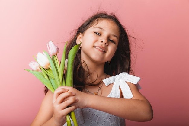 Menina bonitinha segurando um buquê de tulipas em um fundo rosa Feliz dia das mulheres Lugar para texto Emoções vívidas 8 de março