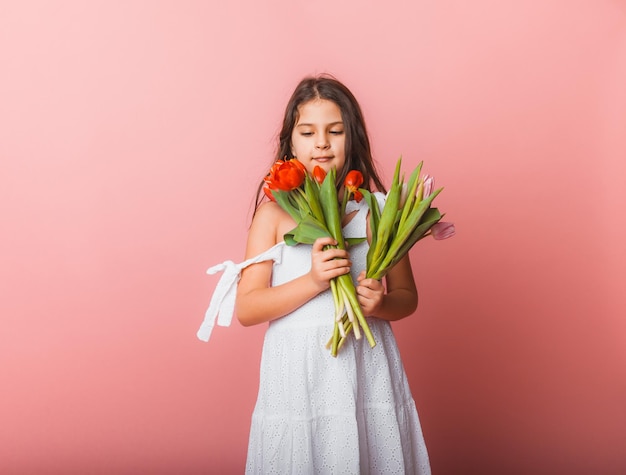 Menina bonitinha segurando um buquê de tulipas em um fundo rosa Feliz dia das mulheres Lugar para texto Emoções vívidas 8 de março