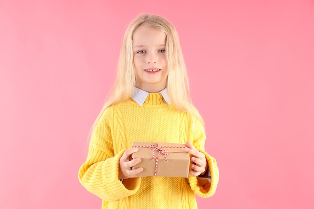 Menina bonitinha segurando uma caixa de presente em fundo rosa