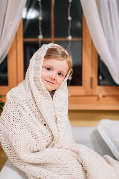 Menina bonitinha senta-se no quarto em um peitoril da janela à noite.