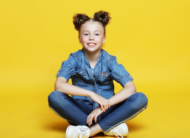 Menina bonitinha sentada e sorrindo isolada em fundo amarelo