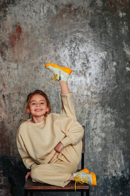 Foto menina bonitinha sentada em uma cadeira no fundo cinza espaço para texto