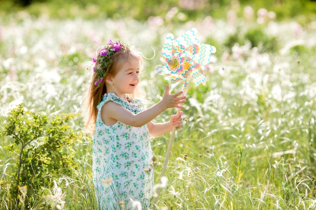 Menina bonitinha sorrindo verão no campo segurando um moinho de vento