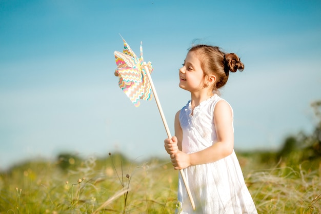 Menina bonitinha sorrindo verão no campo segurando um moinho de vento