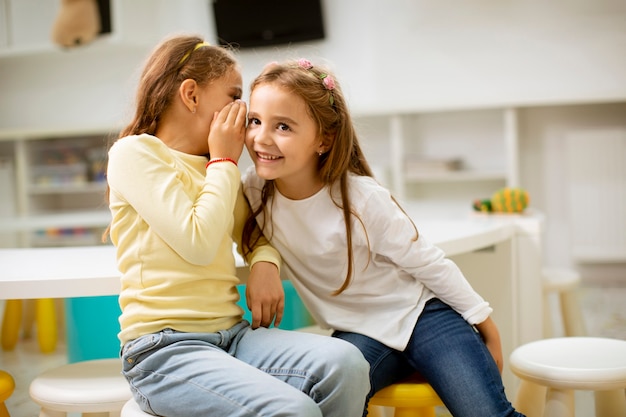 Menina bonitinha sussurrando algo no ouvido de sua amiga